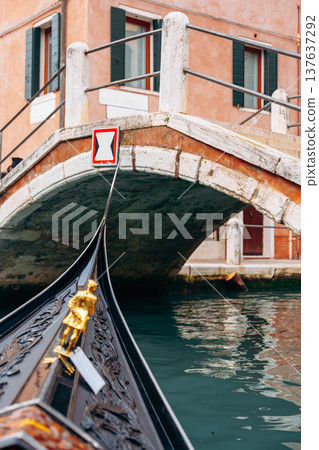 Gondola approaches a bridge in Venice with calm water and rustic buildings around Gondola approaches a bridge in Venice with calm water and rustic buildings around 137637292