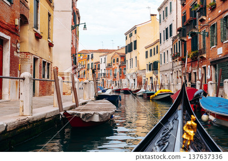Boats and buildings line a quiet canal in Venice during the daytime with clear skies 137637336