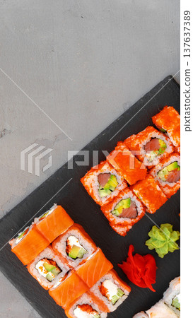 Sushi rolls arranged on a black serving board with garnishes on a gray surface 137637389