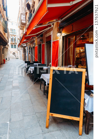 Tables lined up in a narrow street outside restaurants in a famous European city 137637621