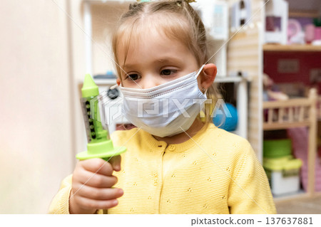 Toddler girl face mask syringe dollhouse smiling waist up 137637881