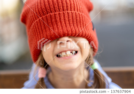 Cheerful girl with red knit cap covering eyes Cheerful girl with red knit cap covering eyes 137637904