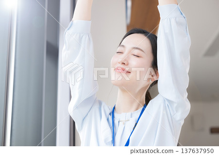 一位女商人坐在辦公室窗邊休息，伸展身體，放鬆身心，周圍環繞著春天清新的綠意。她看起來神清氣爽，精神煥發。 137637950