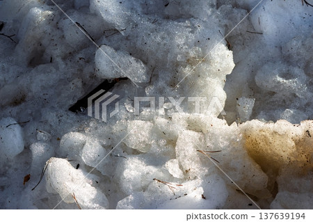 Rough dirty snowdrifts slowly melt by the road, revealing slush and scattered debris. The winter's end brings a textured, granular landscape of thaw and transition into early spring 137639194