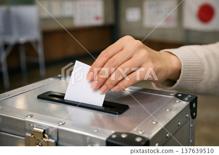 A woman's hand placing a ballot into a ballot box 137639510