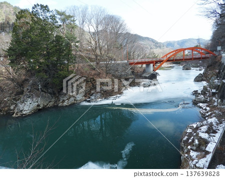 The red Tokiwa Bridge spanning the snow-covered Otaki River and the scenery of the river in early spring. The red Tokiwa Bridge spanning the snow-covered Otaki River and the scenery of the river in early spring. 137639828