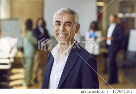 Mature confident business man looking at the camera and smiling in the office. Mature confident business man looking at the camera and smiling in the office. 137641162