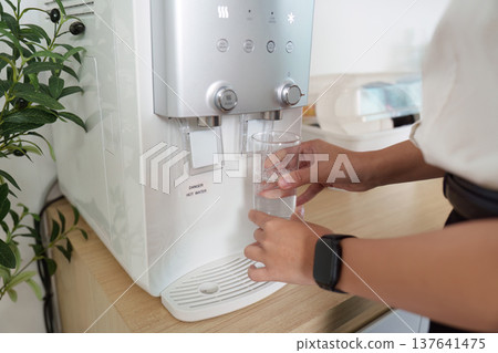 Hydration. Woman filling glass with water from modern water dispenser. 137641475