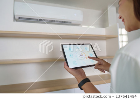 Smart Home Control. Woman using tablet to adjust air conditioning settings. Smart Home Control. Woman using tablet to adjust air conditioning settings. 137641484
