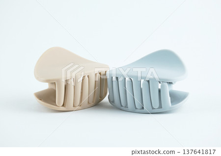Two modern matte plastic hair claw clips in neutral beige and soft blue on a white surface Two modern matte plastic hair claw clips in neutral beige and soft blue on a white surface 137641817