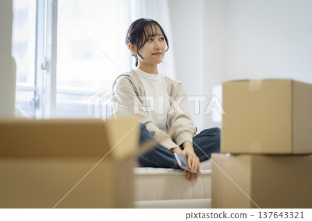 A young woman sitting on a bed mattress surrounded by cardboard boxes. Moving image. A young woman sitting on a bed mattress surrounded by cardboard boxes. Moving image. 137643321