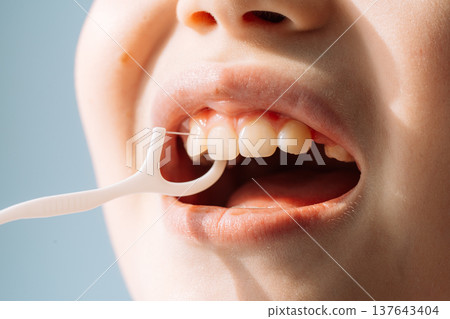 Close up child using a floss pick between teeth, kids dental hygiene routine Close up child using a floss pick between teeth, kids dental hygiene routine 137643404