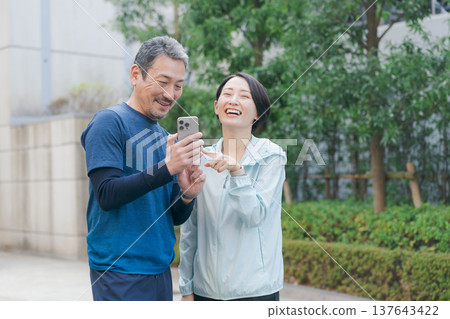 A couple in workout clothes looking at their smartphones A couple in workout clothes looking at their smartphones 137643422