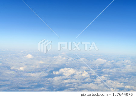 Wide aerial shot of soft white fluffy clouds under a clear bright blue sky during daytime. Breathtaking high altitude view from an airplane window. Peaceful atmospheric nature background. Wide aerial shot of soft white fluffy clouds under a clear bright blue sky during daytime. Breathtaking high altitude view from an airplane window. Peaceful atmospheric nature background. 137644076