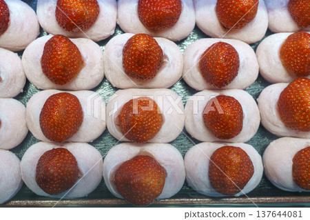 Top-down view of fresh strawberry mochi or ichigo daifuku arranged in neat rows. Each soft pink rice cake is topped with a whole red berry. Authentic Japanese wagashi dessert and sweet snack. 137644081