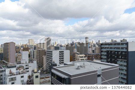 Panoramic high angle view of dense residential apartment buildings in a Japanese city. A metropolitan landscape featuring diverse architecture under a cloudy sky with patches of blue. 137644082