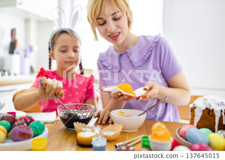 A mother and daughter are happily dyeing and decorating Easter eggs together in a bright kitchen setting A mother and daughter are happily dyeing and decorating Easter eggs together in a bright kitchen setting 137645015