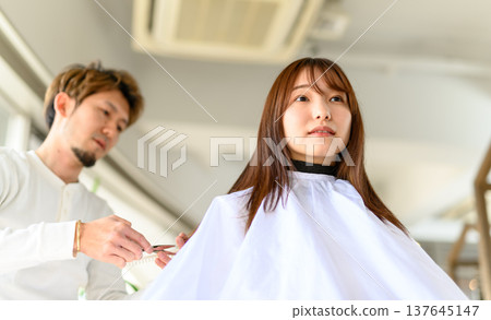 理髮師正在幫一位女顧客剪頭髮。 137645147
