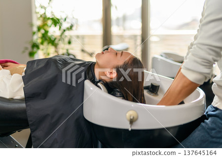 A woman getting her hair washed by a bright window. 137645164