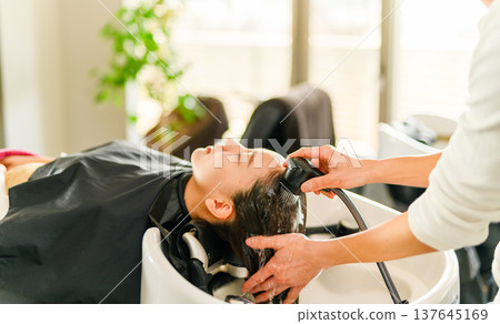 A hairdresser washes a customer's hair. 137645169