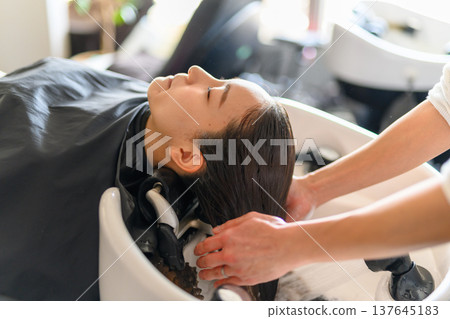 A woman getting her hair washed at the shampoo station. A woman getting her hair washed at the shampoo station. 137645183