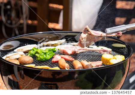 Grilling meat on a barbecue and picking it up with tongs Grilling meat on a barbecue and picking it up with tongs 137645457