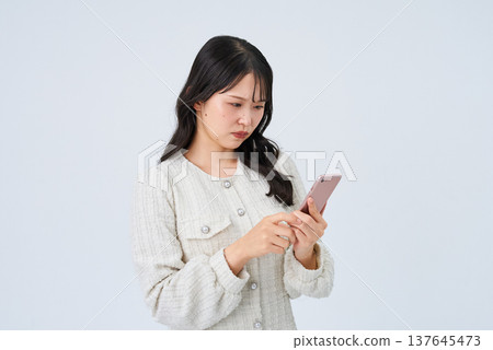 一位年輕女子帶著不安的表情看著智能手機屏幕 一位年輕女子帶著不安的表情看著智能手機屏幕 137645473