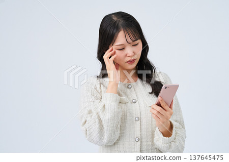 一位年輕女子帶著不安的表情看著智能手機屏幕 一位年輕女子帶著不安的表情看著智能手機屏幕 137645475