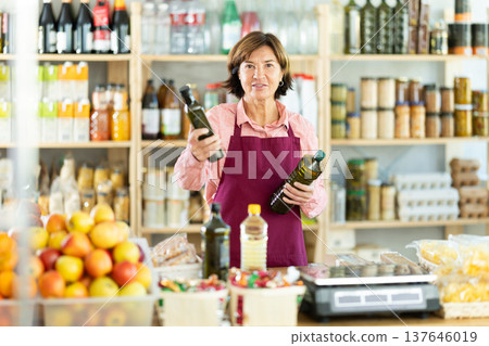 Experienced female salesperson offers choice of buying bottle of vegetable oil or olive oil in grocery store Experienced female salesperson offers choice of buying bottle of vegetable oil or olive oil in grocery store 137646019