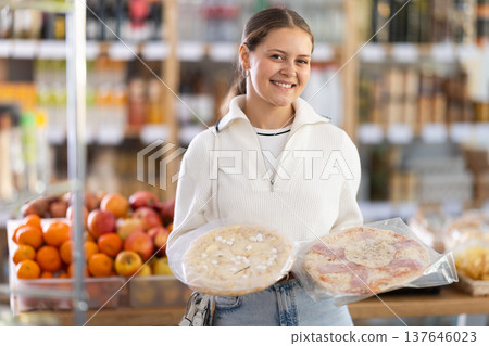 Female buyer carefully reads labels on frozen pizza - she chooses the best product in supermarket Female buyer carefully reads labels on frozen pizza - she chooses the best product in supermarket 137646023