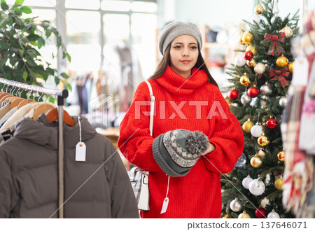 Girl spend time in shop and choose knitted hat, X mas discount season 137646071