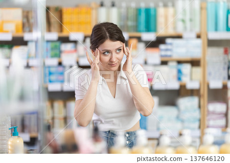 Girl with headache looking for pain relief medicine in pharmacy Girl with headache looking for pain relief medicine in pharmacy 137646120