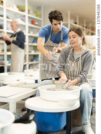 Young man helping young woman shape pottery on wheel Young man helping young woman shape pottery on wheel 137646166