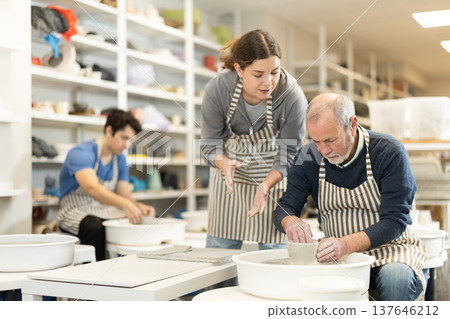 Girl help to mature man working on potters wheel in pottery workshop 137646212