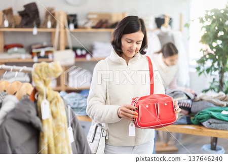 Woman looks at products in store and selects handbag. 137646240