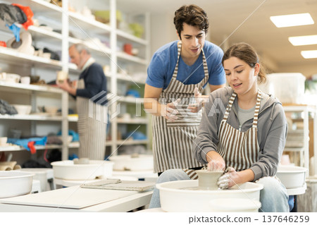 Young man helping young woman shape pottery on wheel Young man helping young woman shape pottery on wheel 137646259