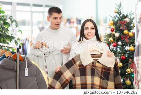 Young couple choosing coat or jacket for girl in clothing store Young couple choosing coat or jacket for girl in clothing store 137646262