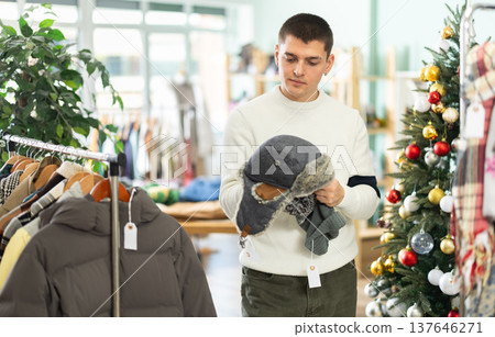 Young guy choosing winter hat in clothing store Young guy choosing winter hat in clothing store 137646271