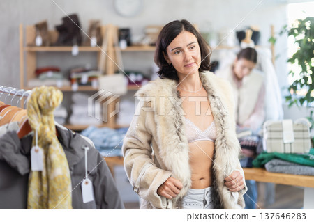 Woman try on fur jacket in front of mirror in clothes store, semi naked body Woman try on fur jacket in front of mirror in clothes store, semi naked body 137646283