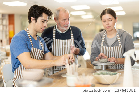 Eldery man helping young guy sculpting ceramic piece Eldery man helping young guy sculpting ceramic piece 137646391