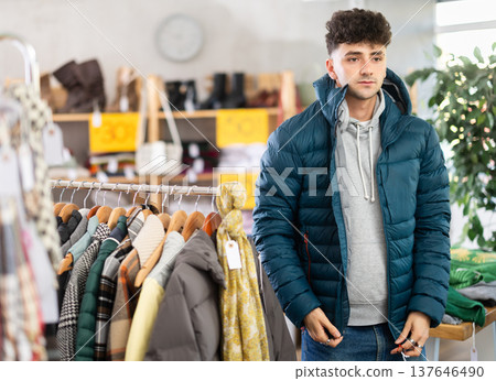 Guy try on down jacket in front of mirror in clothes store 137646490