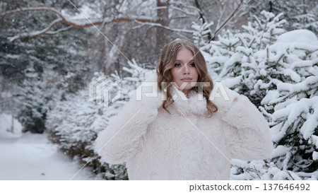 Fashionable woman wearing white fur coat standing among snow covered trees, embodying winter elegance with serene woodland backdrop Fashionable woman wearing white fur coat standing among snow covered trees, embodying winter elegance with serene woodland backdrop 137646492