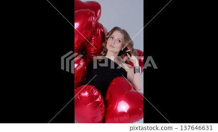 Glamorous woman posing confidently amid shiny red heart shaped balloons, radiating romantic elegance and celebratory mood 137646631