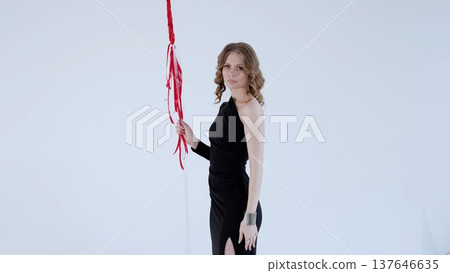 Fashion model wearing sleek black dress, standing amid red and white ribbons cascading from studio ceiling, embodying elegant celebration with dynamic pose 137646635