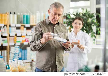 Senior man buys antibacterial ointment at drug store, girl pharmacist in background Senior man buys antibacterial ointment at drug store, girl pharmacist in background 137646638