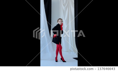 Stylish female model posing in vibrant red gloves, tights, black jacket, high heels against monochromatic curtain background, highlighting dramatic fashion contrast and textural elements Stylish female model posing in vibrant red gloves, tights, black jacket, high heels against monochromatic curtain background, highlighting dramatic fashion contrast and textural elements 137646643