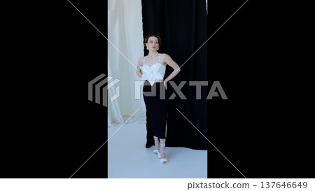Fashion model wearing white top with bow detail, paired with sleek black skirt, standing against minimalist black white background, embodying contemporary elegance Fashion model wearing white top with bow detail, paired with sleek black skirt, standing against minimalist black white background, embodying contemporary elegance 137646649
