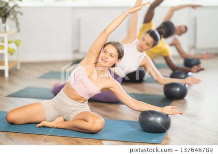 Young woman doing Mermaid Stretch with Ball in pilates class 137646789