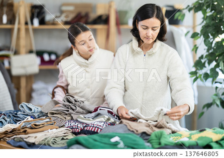 Mother and teen daughter looks at products in store and selects knitted jumper. Mother and teen daughter looks at products in store and selects knitted jumper. 137646805