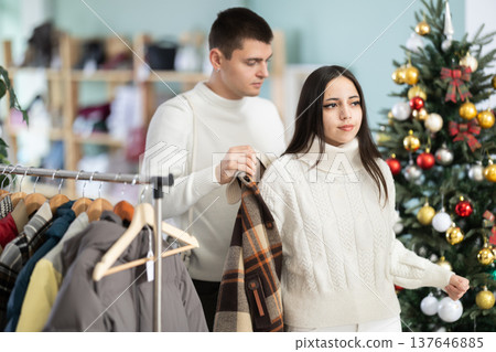 Girl tries on plaid jacket accompanied by guy in shop, X mas eve 137646885